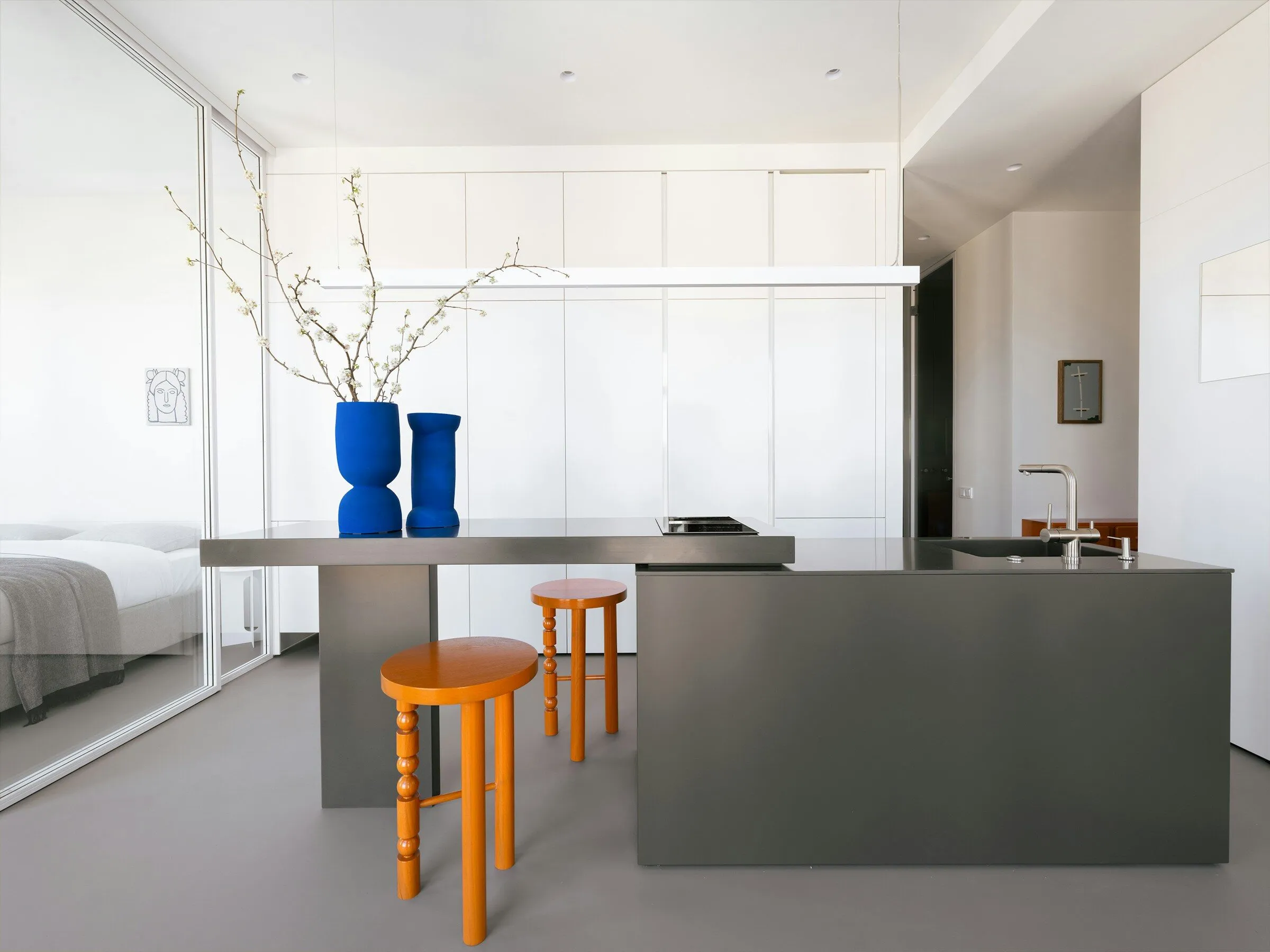 Open kitchen with a grey steel island, orange stools and blue vases on the counter