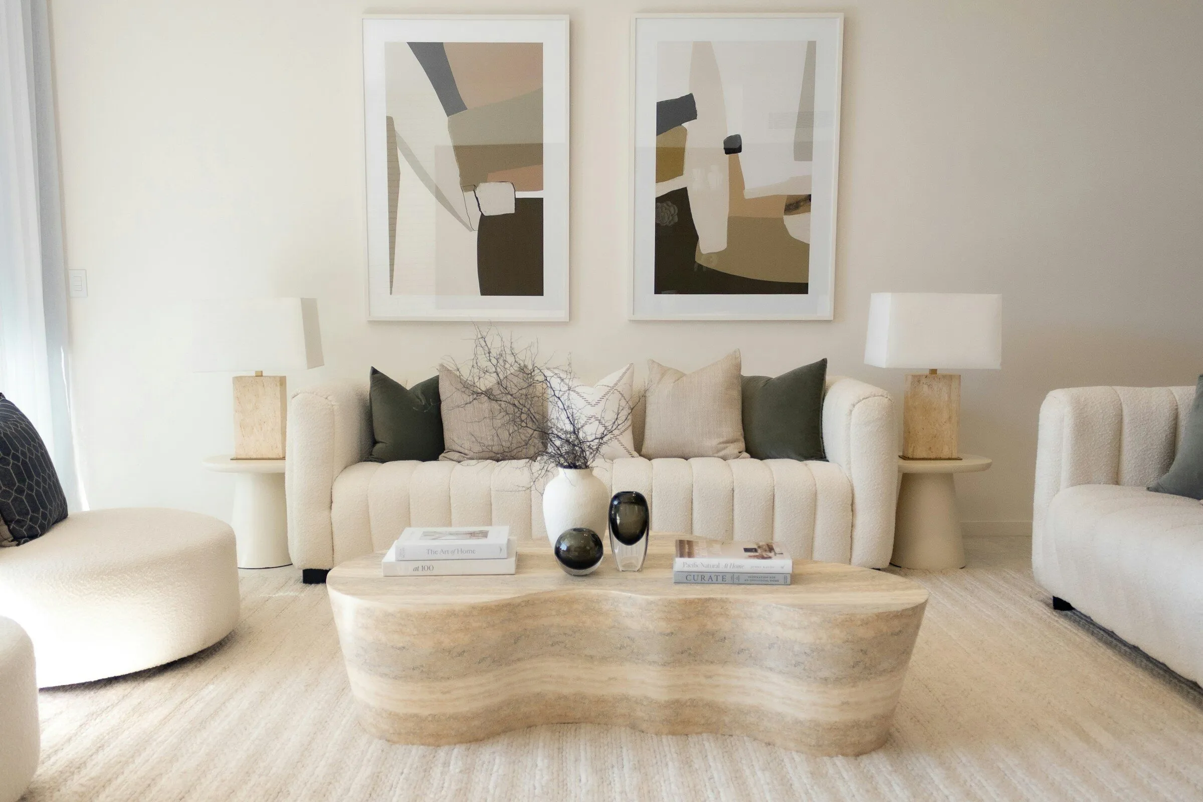 Living room in cream tones with a curved sofa, a travertine table and two framed prints