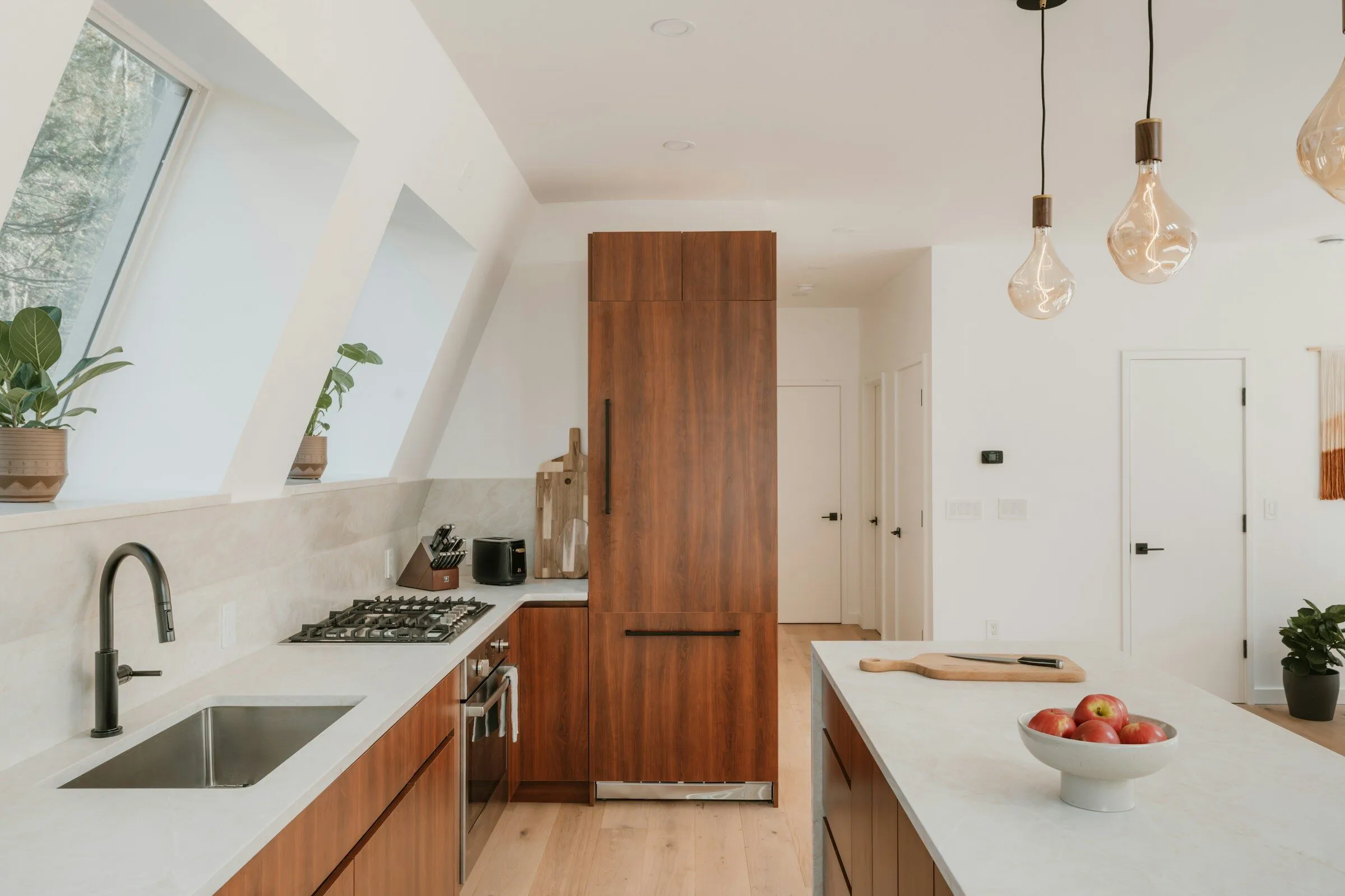 Kitchen with walnut cabinets, a pale stone worktop and pendant bulbs
